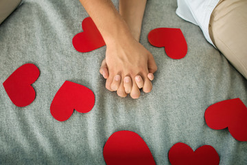 Young couple with red hearts holding hands while lying on bed at home