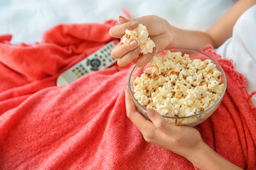 Young woman eating popcorn while watching TV in bedroom, closeup