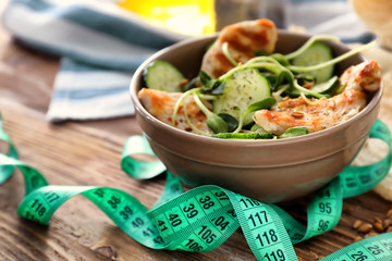 Bowl with tasty chicken salad and measuring tape on wooden table. Diet concept