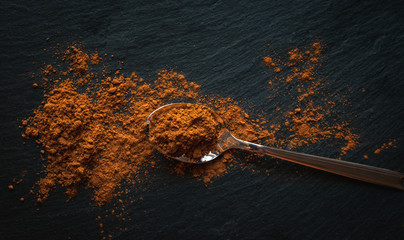 Ground cinnamon in teaspoon on dark background, top view, text space