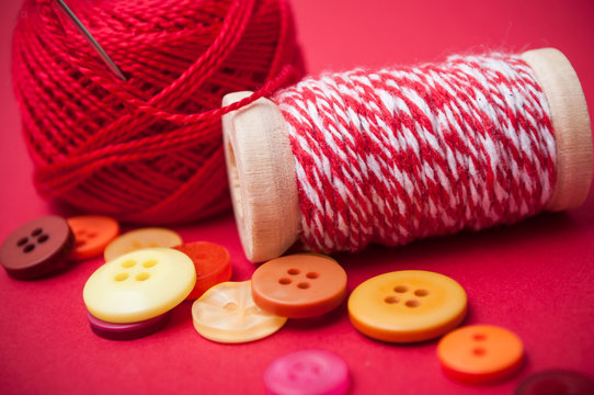 closeup of buttons and bobbins of cotton yarn on red background