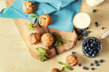 Wooden board with tasty blueberry muffins on light table