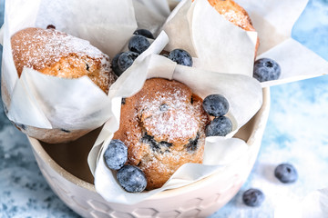 Bowl with blueberry muffins on color table