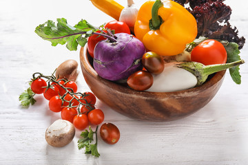 Bowl with different fresh vegetables on light wooden table