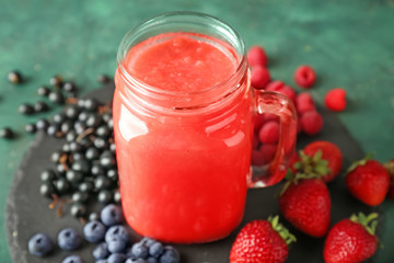 Mason jar of tasty red smoothie and berries on slate plate