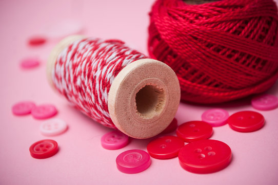 closeup of buttons and bobbins of cotton yarn on pink background