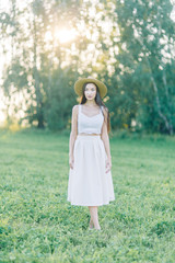 Girl walking on the field, in a hat and summer dress. Smiling and laughing, beautiful sunset in the forest and in nature. White dress and rye, sloping fields. Happy traveler, lifestyle.