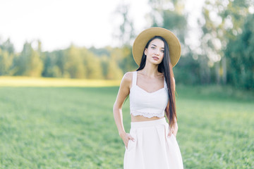 Girl walking on the field, in a hat and summer dress. Smiling and laughing, beautiful sunset in the forest and in nature. White dress and rye, sloping fields. Happy traveler, lifestyle.