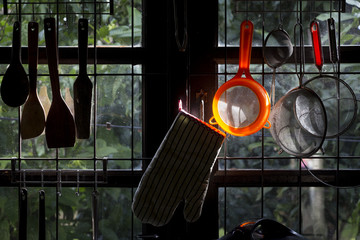 Cooking utensils hanging on a kitchen window with beautiful sunlight glowing on an orange plastic sieve