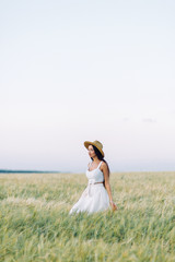Fototapeta na wymiar Girl walking on the field, in a hat and summer dress. Smiling and laughing, beautiful sunset in the forest and in nature. Happy traveler, lifestyle.