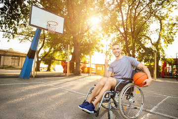 Young man with ball sitting in wheelchair outdoors