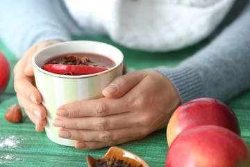 Woman holding cup of delicious mulled wine on color wooden table, closeup