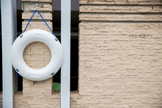 lifebuoy, all water rescue emergency equipment. white lifebuoy on brick wall. nearby the swimming pool, image for background, wallpaper, objects and copy space. for safety and rescue.