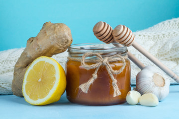Garlic, a honey jar, ginger, lemon and honey spoons on a blue background. Maintenance of immunity. Treatment of colds and flu. Products for immunity. Immunity concept.