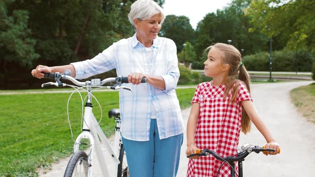 family, leisure and people concept - happy grandmother and granddaughter with bicycles at summer park