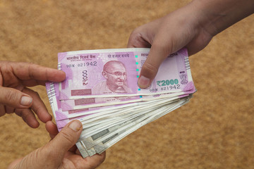 Hand Giving Indian 500 and 2000 Rupee Bank Notes over wheat background. concept for earnings or spend in Agriculture.