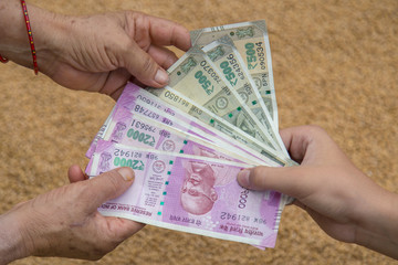 Hand Giving Indian 500 and 2000 Rupee Bank Notes over wheat background. concept for earnings or...
