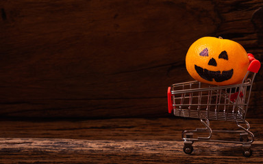 Fresh Orange with Halloween Pumpkins painted face on shopping cart on wood background.