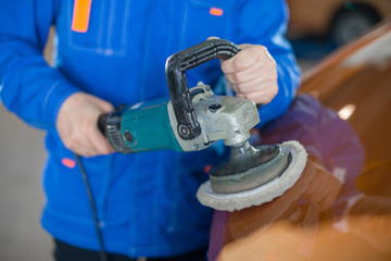 a man with an electric tool polishes the body of the car