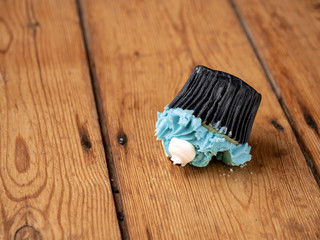 A cupcake with blue icing that has been dropped upside down onto a wooden floor