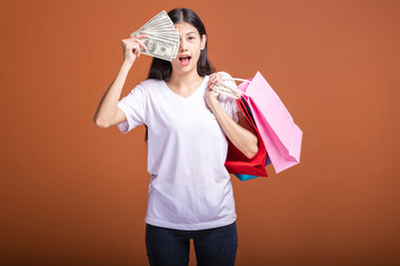 Woman holding shopping bag and cash isolated in orange background.