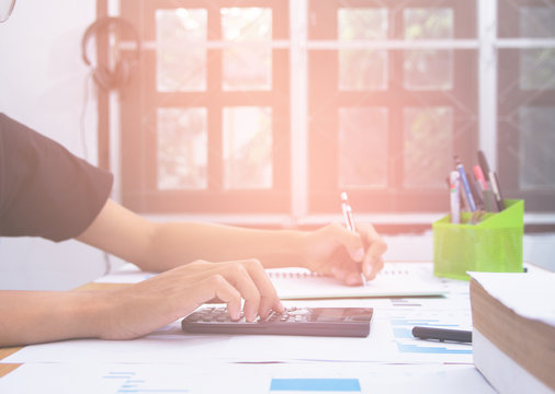 Business man or accountant in gray shirt holding pen working on accounts and using calculator and writing on desk, With sunset light.