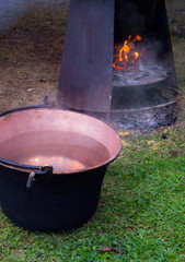 Hot water into a big copper pot next to fire