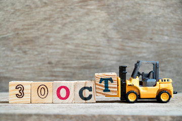 Toy forklift hold block T to complete word 30 oct on wood background (Concept for calendar date in...