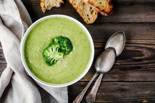 Homemade broccoli cream soup in white bowl with toasts on wooden background