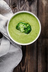 Homemade broccoli cream soup in white bowl with toasts on wooden background