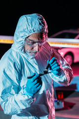 male criminologist in protective suit and latex gloves taking fingerprints from knife at crime scene