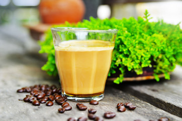 Hot latte coffee is placed on an old wooden table near the moss tray and coffee beans on the floor. .See the glass and coffee beans more clearly than anything else.