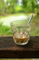 Half a glass of coffee on an old wooden terrace in a garden.