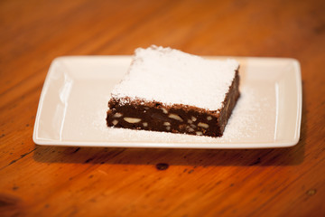 a brownie on a square plate with powdered sugar on top