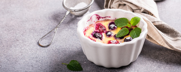 Berry clafouti. Traditional french sweet fruit dessert clafoutis with raspberries and blueberries on gray concrete background. Healthy gluten free food concept with copy space. Banner.