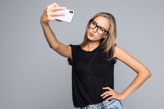 Happy cute woman making selfie on phone over gray background.