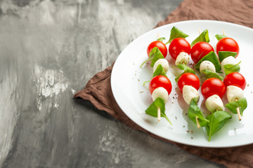 Salad Caprese - shish kebab with tomato, mozzarella and basil, Italian cuisine and a healthy vegetarian diet on a dark background. with copy space, top view, flat lay