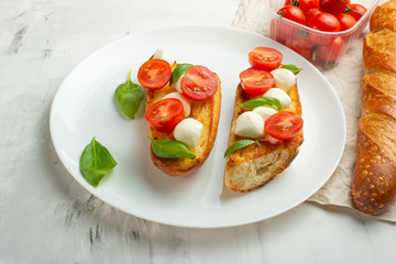 Bruschetta with tomatoes, mozzarella cheese and basil on a light background in a white plate. flat lay
