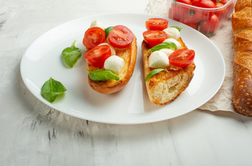 Bruschetta with tomatoes, mozzarella cheese and basil on a light background in a white plate. flat lay