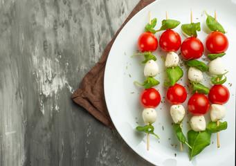 Salad Caprese - shish kebab with tomato, mozzarella and basil, Italian cuisine and a healthy vegetarian diet on a dark background. with copy space, top view, flat lay