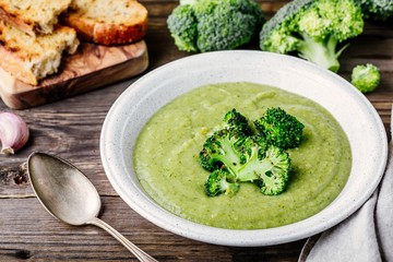 Homemade broccoli cream soup in white bowl with toasts on wooden background