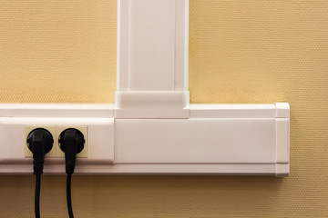White cable channel with electrical outlets on a yellow wall, where two black plugs are inserted.