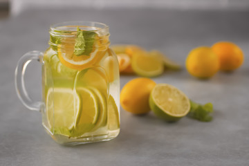 Refreshing lemonade with lemon and lime slices and mint leaves in a glass mug on a gray background.