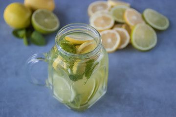 Refreshing lemonade with lemon and lime slices and mint leaves in a glass mug on a gray background. Soft focus.