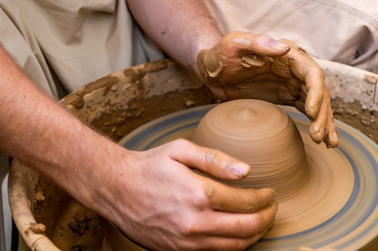 Hands of a young man creating a clay jar on a potter's wheel