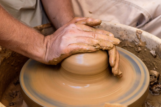 Hands of a young man creating a clay jar on a potter's wheel
