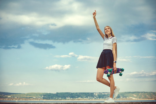 Cute girl is standing with her skateboard in hands. Street life. Urban style of life. Youth culture. Urban sport. Instagram style image. A lot of space for text.