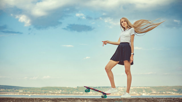 Cute girl is standing with her skateboard in hands. Street life. Urban style of life. Youth culture. Urban sport. Instagram style image. A lot of space for text.