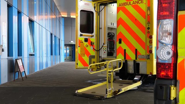 Two ambulance vehicles by the hospital accident and emergency door. Rear door is open and access lift ramp light is flashing