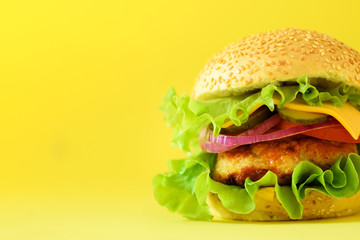 Macro view of tasty burger with beef, cheese, lettuce, onion, tomatoes on yellow background. Close up banner. Unhealthy diet concept and copy space